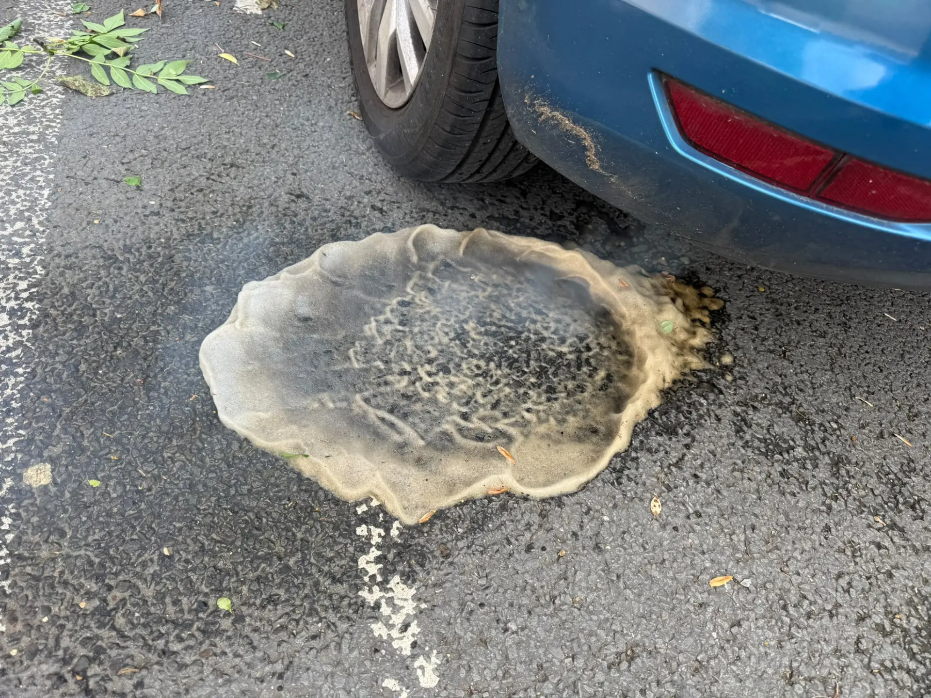 Dark soot-filled cleaning residue discharged from the exhaust of a blue vehicle during a professional DPF cleaning service.