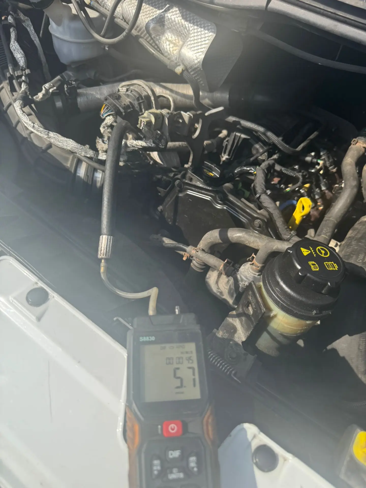 Ford Transit engine bay during DPF diagnostic testing, with a digital manometer displaying an initial pressure reading of 5.7 mbar.