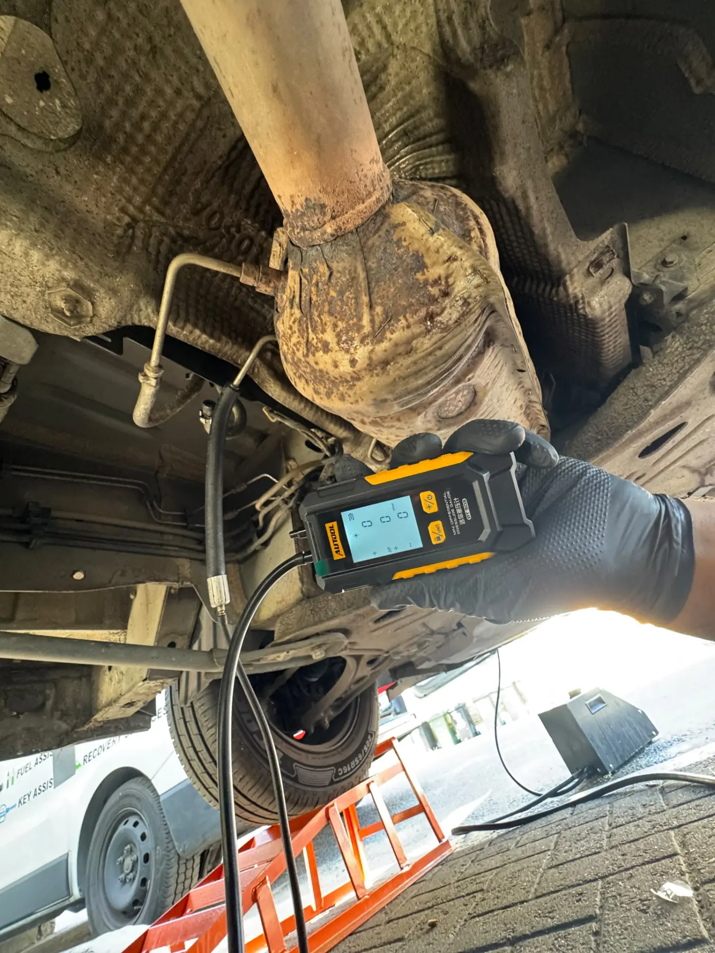 Technician using a DPF pressure testing device under a vehicle during a diesel particulate filter inspection.