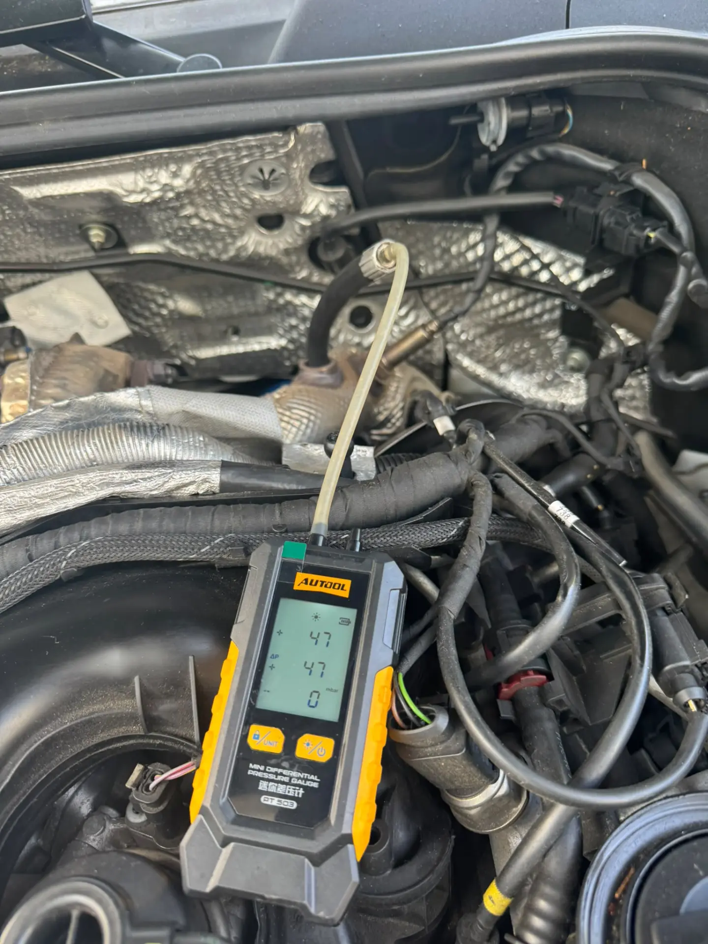 Technician measuring the Porsche Cayenne's DPF differential pressure before cleaning, showing a 47 mbar reading on a digital diagnostic gauge.