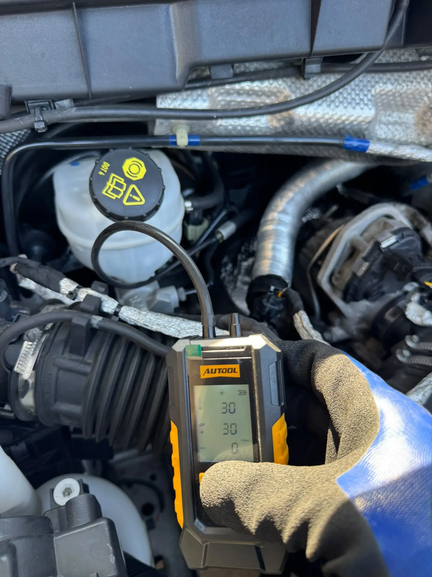 A handheld differential pressure gauge showing a DPF pressure reading of 30 mbar during vehicle diagnostics.