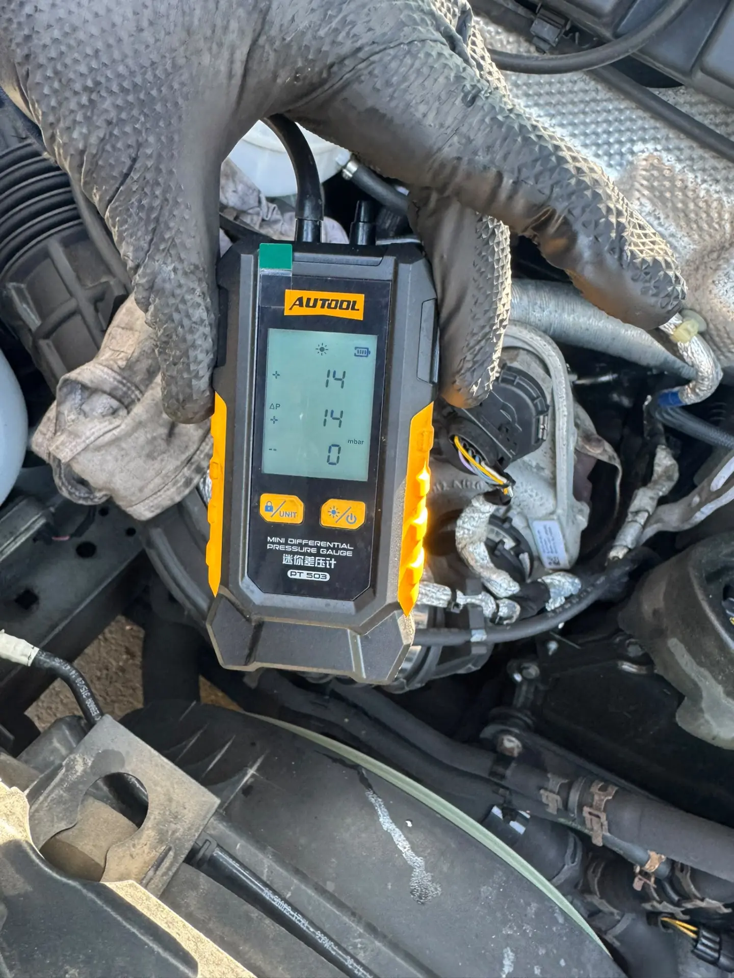 A handheld differential pressure gauge showing a DPF pressure reading of 14 mbar during vehicle diagnostics.