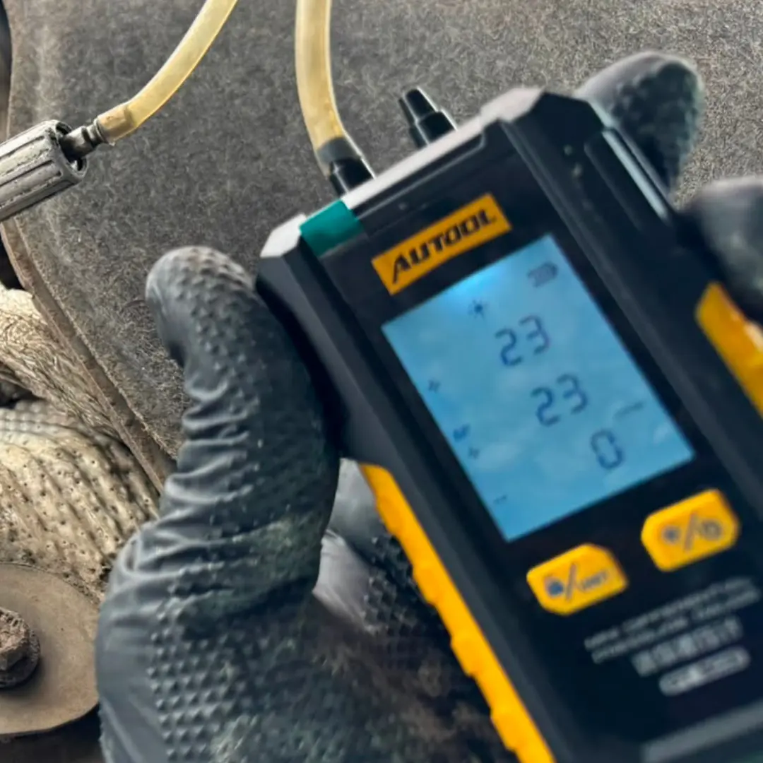 Technician using a digital differential pressure gauge to measure DPF back pressure beneath a vehicle prior to DPF cleaning.