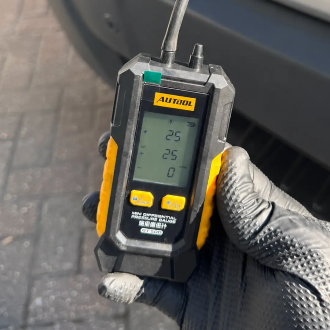 Gloved hand holding a digital pressure gauge showing 25 mbar before Ford Transit DPF cleaning.