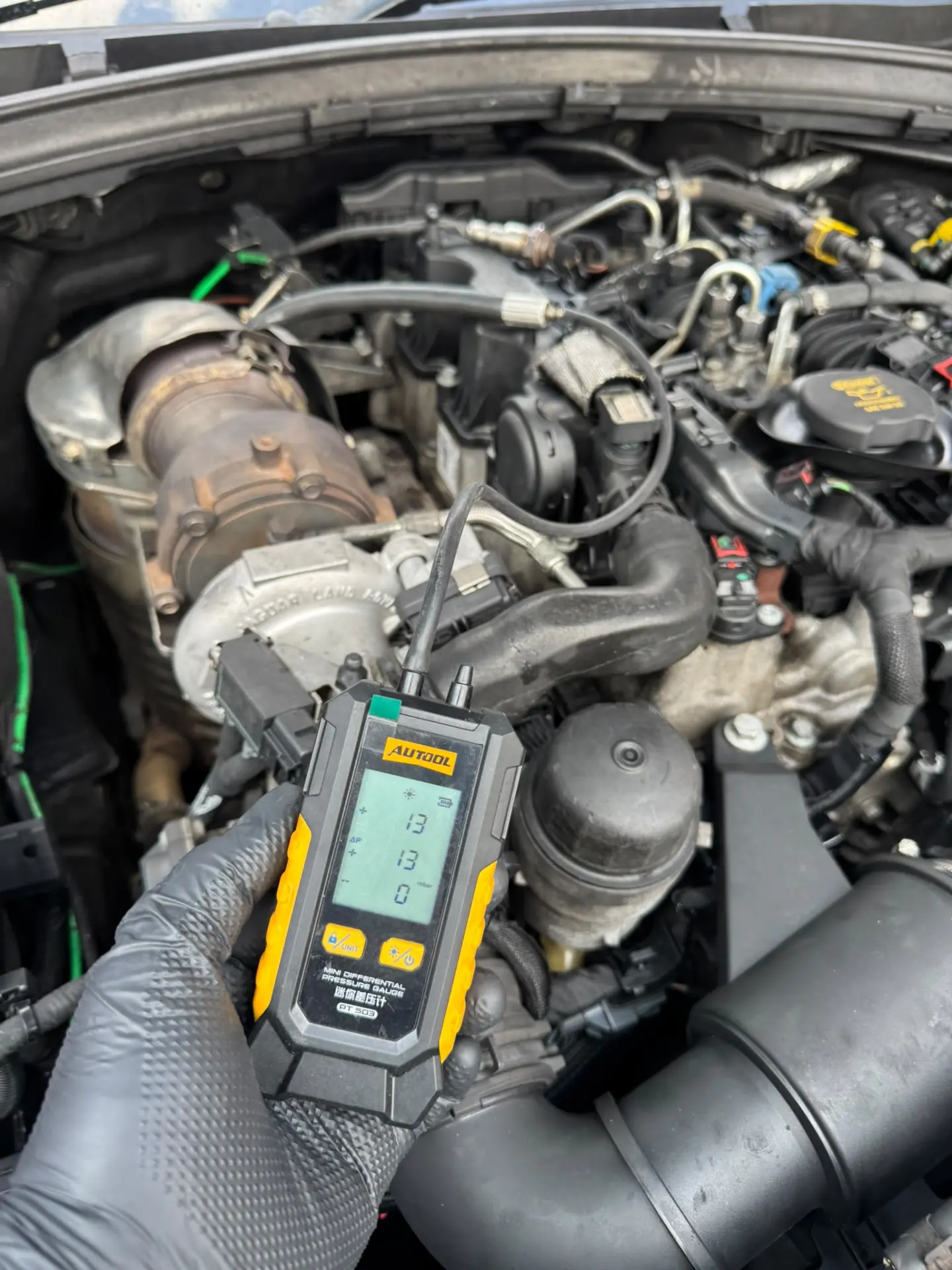 Mechanic using a digital differential pressure gauge to diagnose a diesel particulate filter and check exhaust pressure.